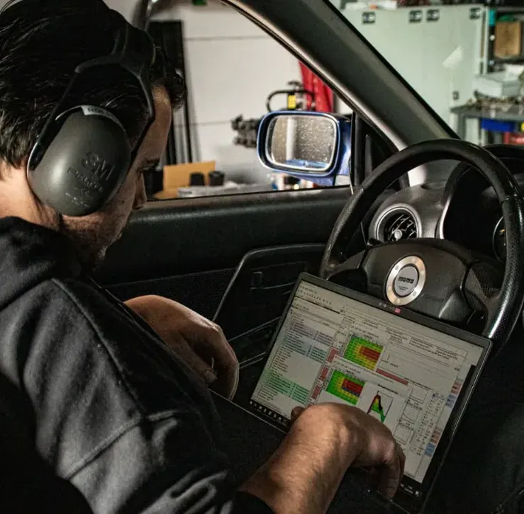 Monteur met gehoorbescherming bekijkt brandstof- en ontstekingsmaps op een laptop in de auto tijdens ECU-calibratie.