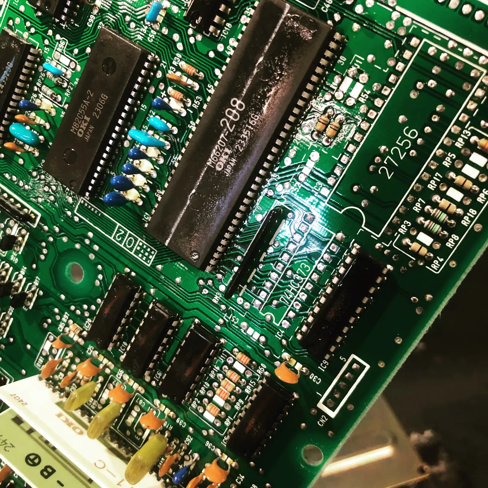Macro-opname van een groene printplaat met OKI-chips en weerstanden tijdens elektronicarevisie.