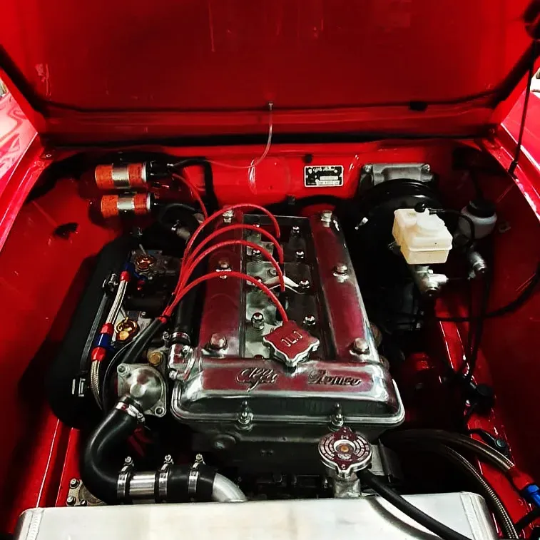 Motorruimte van een klassieke Alfa Romeo met gepolijst kleppendeksel en rode ontstekingskabels.