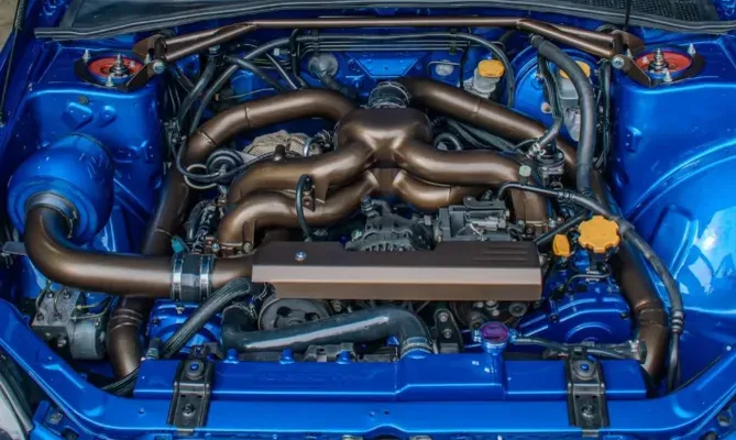 Motorruimte van een blauwe Subaru met een op maat gemaakt bronskleurig uitlaatspruitstuk en grote turbo.