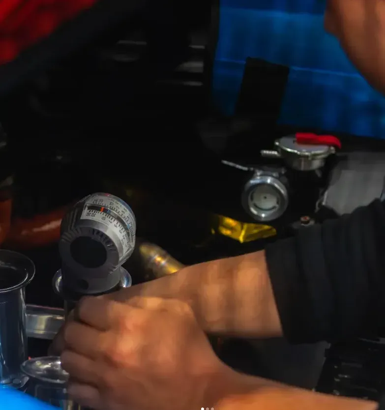 Monteur stelt handmatig een brandstofmeetinstrument af boven een maatbeker tijdens calibratiewerk.